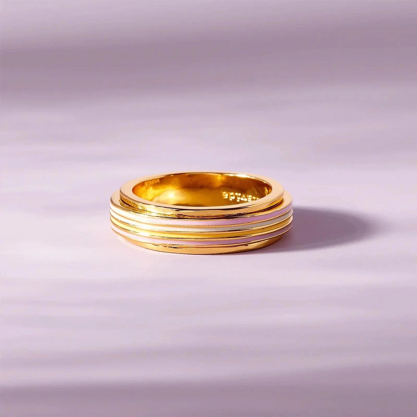 Gold ring with pink interior on a light purple background