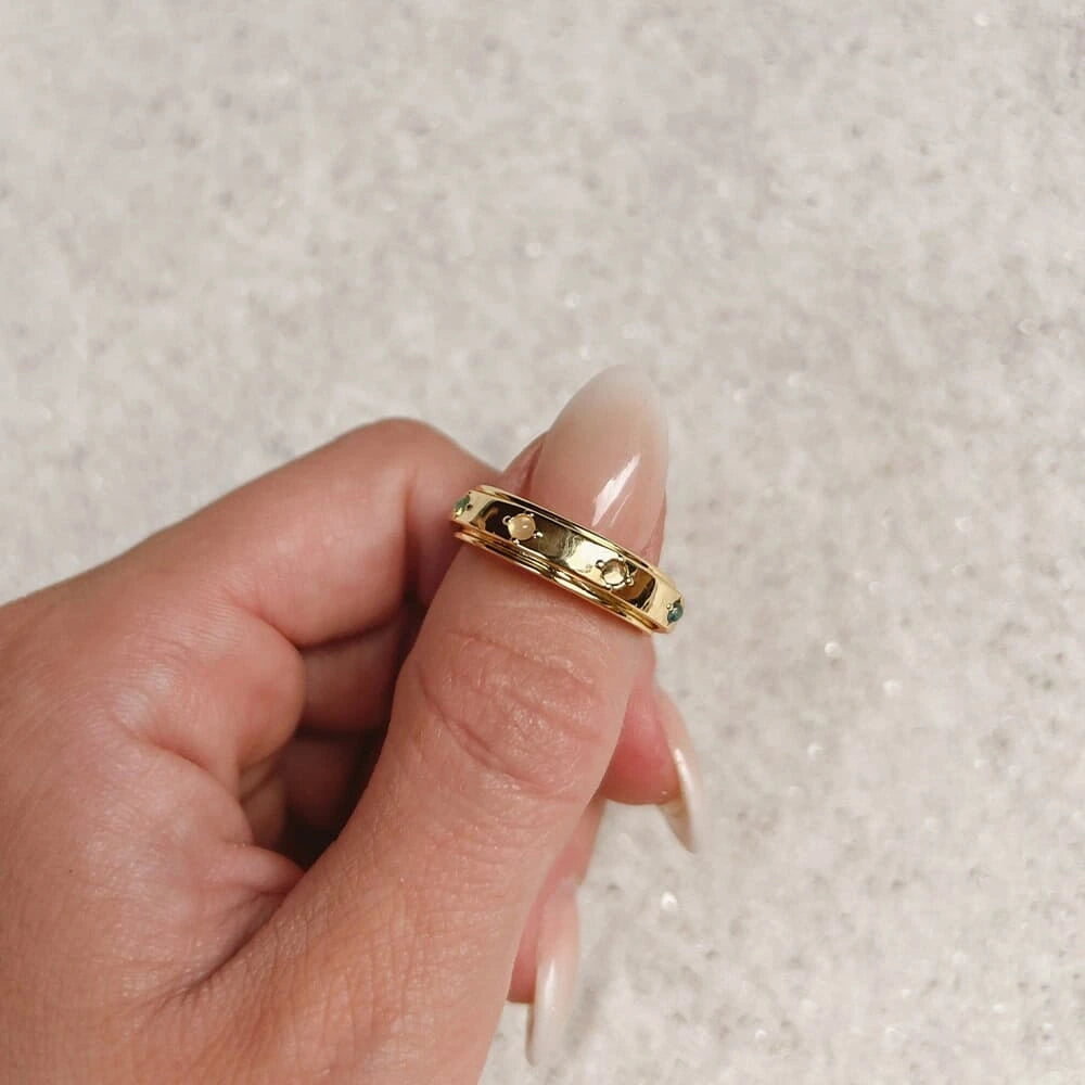 Gold ring with small stones on a finger against a neutral background