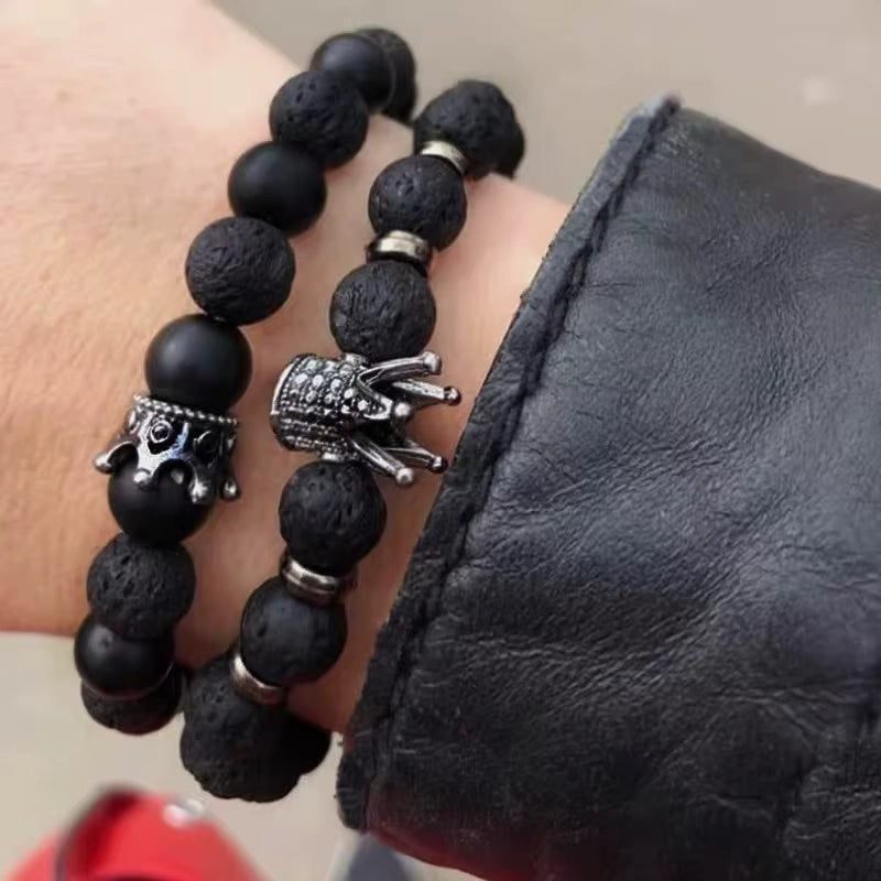 Black beaded bracelet with silver charms on a wrist, against a black leather sleeve.