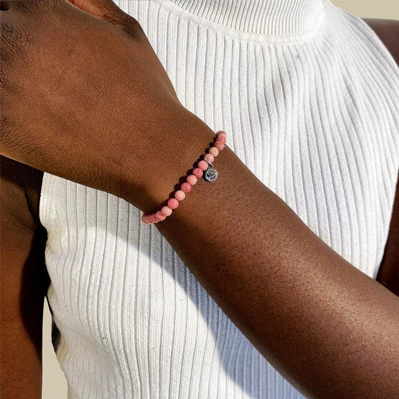 Person wearing a pink beaded bracelet on a white ribbed sleeve
