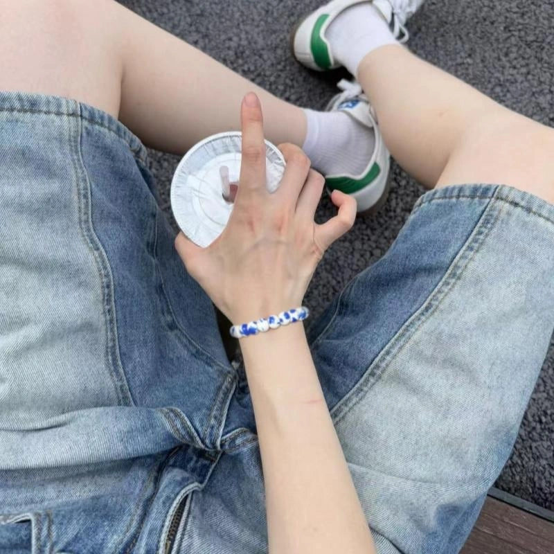 Person wearing denim shorts and white sneakers with green accents, sitting on a textured surface.