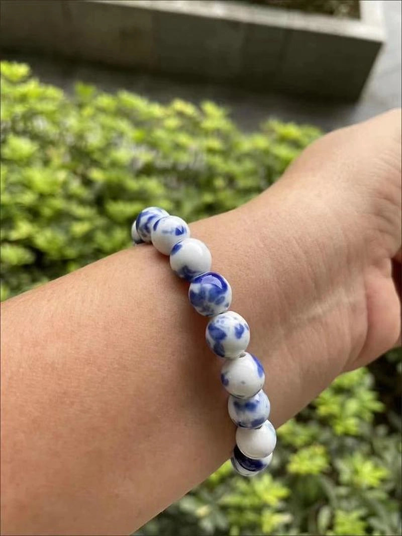 White and blue beaded bracelet on a wrist with a blurred green background
