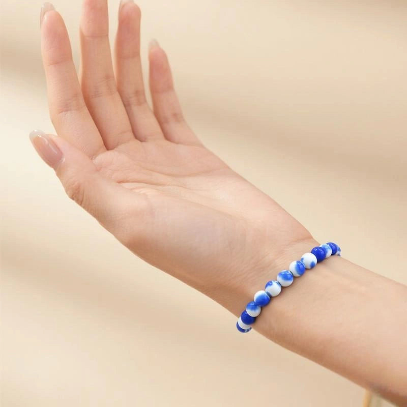 Hand wearing a blue and white beaded bracelet on a beige background