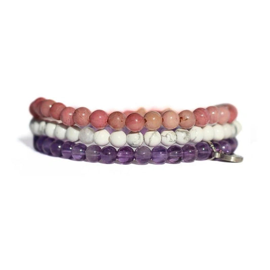 Set of three beaded bracelets in pink, white, and purple on a white background