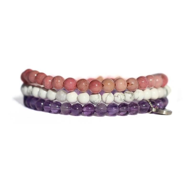 Set of three beaded bracelets in pink, white, and purple on a white background