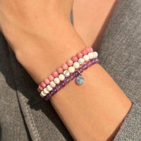 Close-up of a wrist wearing two beaded bracelets on a gray background