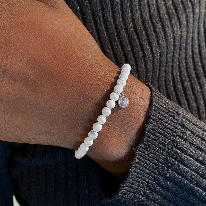 White beaded bracelet on a wrist with a dark textured sleeve