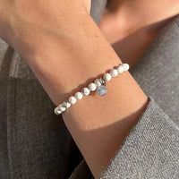 Close-up of a wrist wearing a beaded bracelet with a small round charm.