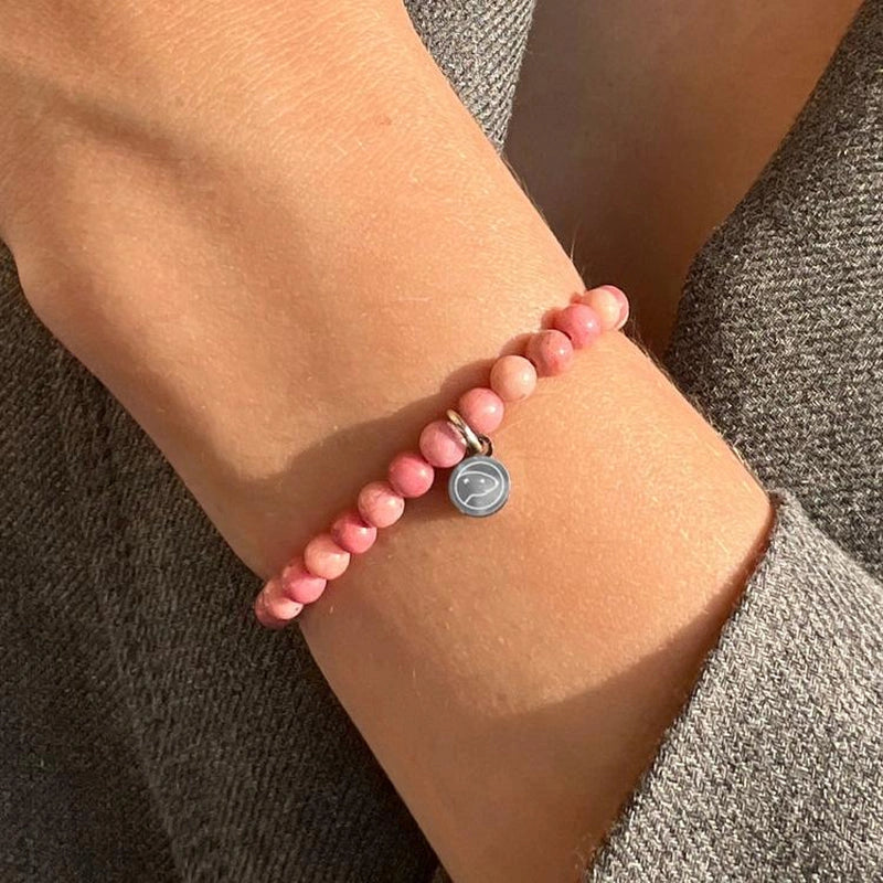 Pink beaded bracelet with a gray charm on a wrist against a neutral background